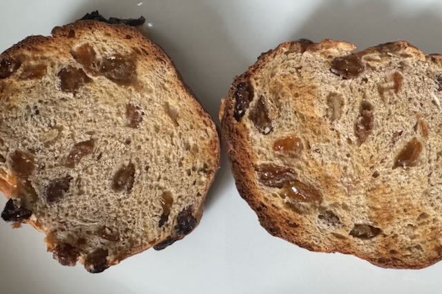 A cross-section of two halves of hot cross bun, toasted but not yet buttered, on a white plate