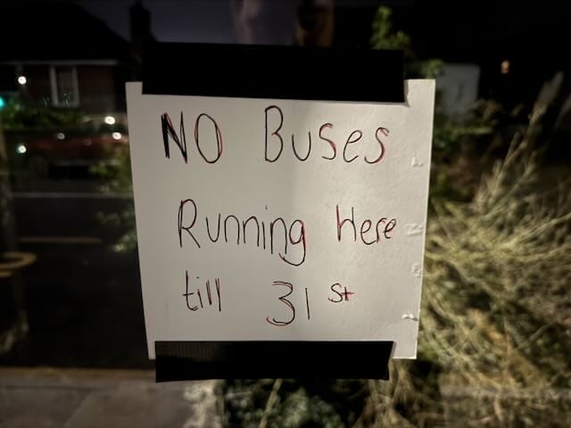 handwritten sign saying No Buses Running Here till 31st, gaffer-taped to a glass bus shelter